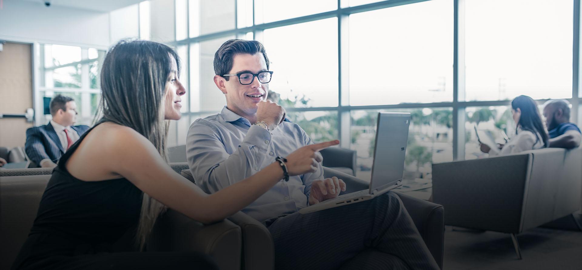 Two people sitting on couch talking and looking at laptop