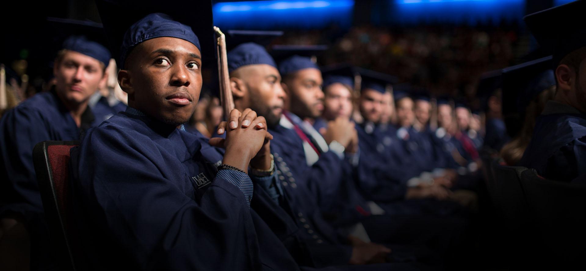 Student in cap and gown sitting down at graduation ceremony